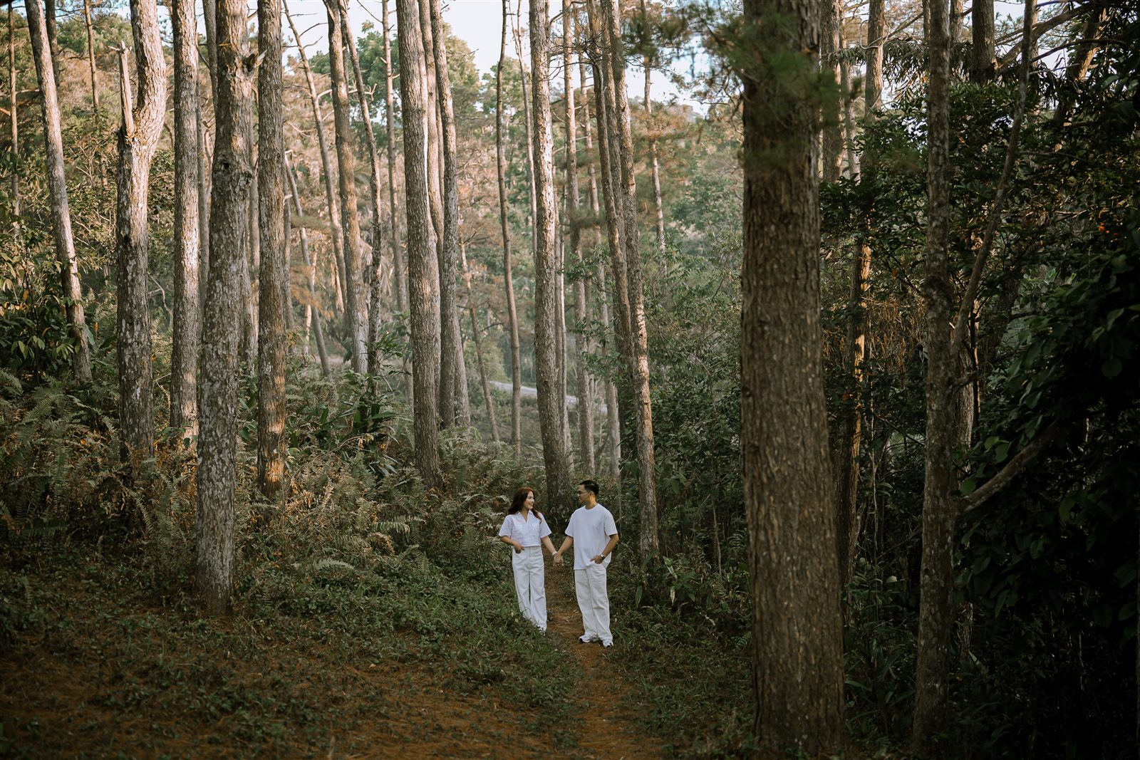 Caren and Zayrol walking hand in hand through the pine forest